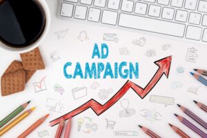 A desk setup with a keyboard, pencils, a cup of coffee, and a red arrow pointing upwards. Text on the image reads "AD CAMPAIGN" and "Search". This image could represent the growth of a responsive search ad campaign.