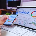 AdWords Manager analysing ROI on laptop and smartphone with various graphs and charts displayed, improving digital marketing results.