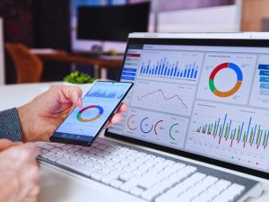 AdWords Manager analysing ROI on laptop and smartphone with various graphs and charts displayed, improving digital marketing results.