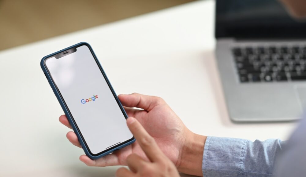 A person using a smartphone with the Google search page open, highlighting the importance of Google Ads for mobile optimisation.