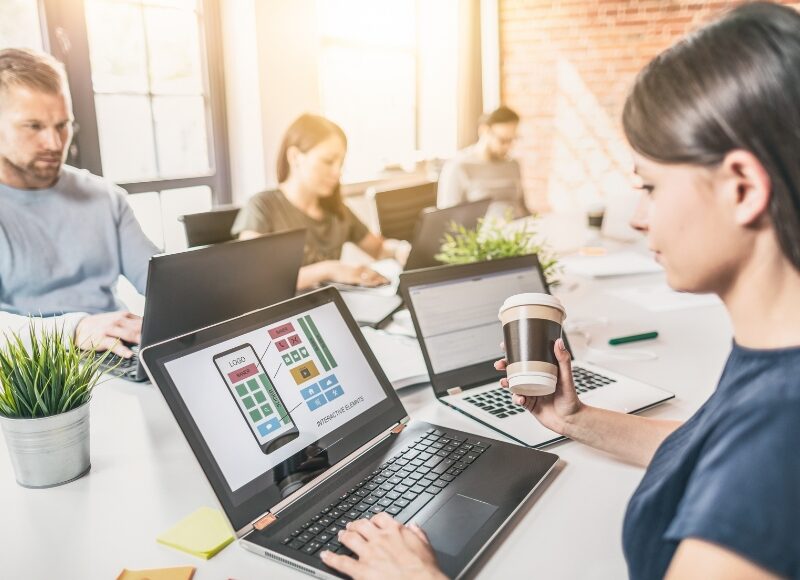 Team working on laptops in a bright office, focusing on how to design a business website interface.