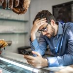 Frustrated man looking at smartphone in a store, wondering why Google Ads are not showing up.