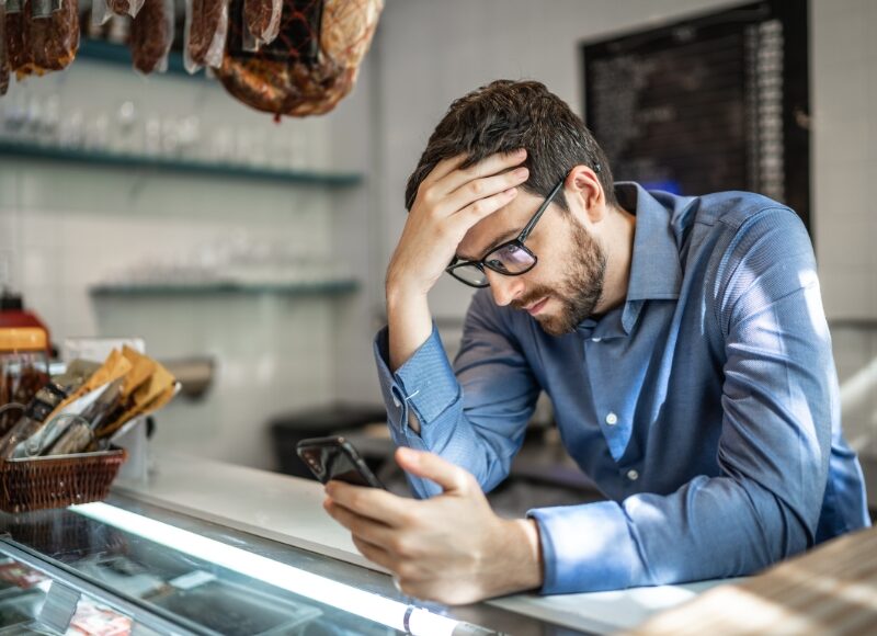 Frustrated man looking at smartphone in a store, wondering why Google Ads are not showing up.