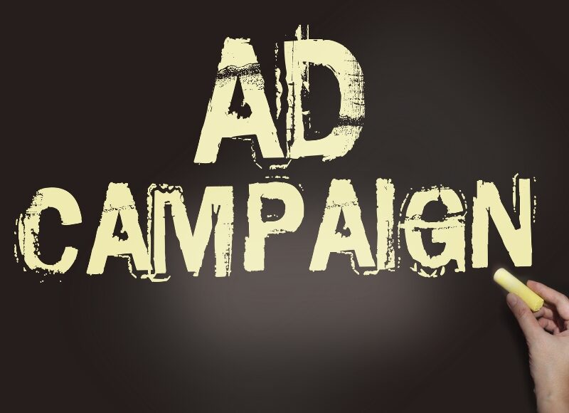 Hand writing “AD CAMPAIGN” on a chalkboard, symbolising creative planning for seasonal campaigns in advertising.