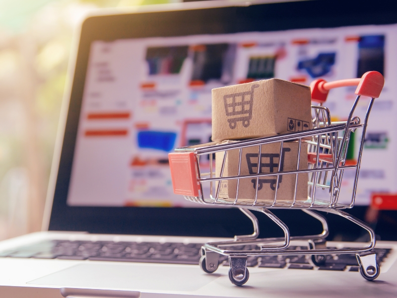 Small shopping cart with cardboard parcels on a laptop screen used to advertise Google Shopping products online.