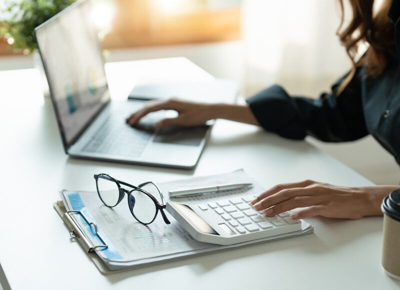 Professional analysing reports and budget on laptop and calculator for Google Ads Management performance tracking.