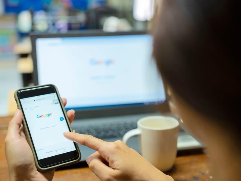 Person using Google on a smartphone while working on a laptop, showing how a google ads service supports online visibility.