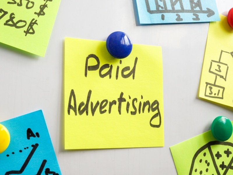 Yellow sticky note on a board with “Paid Advertising” written in marker, used to explain paid Google advertising concepts.