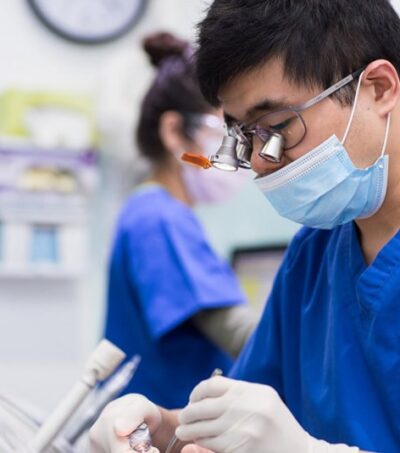 Dentist performing implant treatment in clinic while wearing blue scrubs and mask