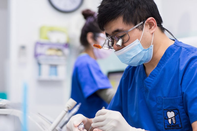 Dentist performing implant treatment in clinic while wearing blue scrubs and mask