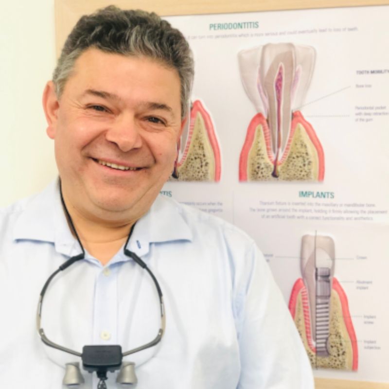 Dentist standing in clinic with dental implant and periodontitis display behind him