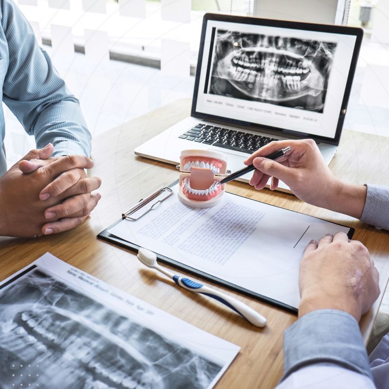 Digital Marketing for Dentists: Dentist explaining dental care using tooth model and x-ray, illustrating patient education strategies for online marketing.