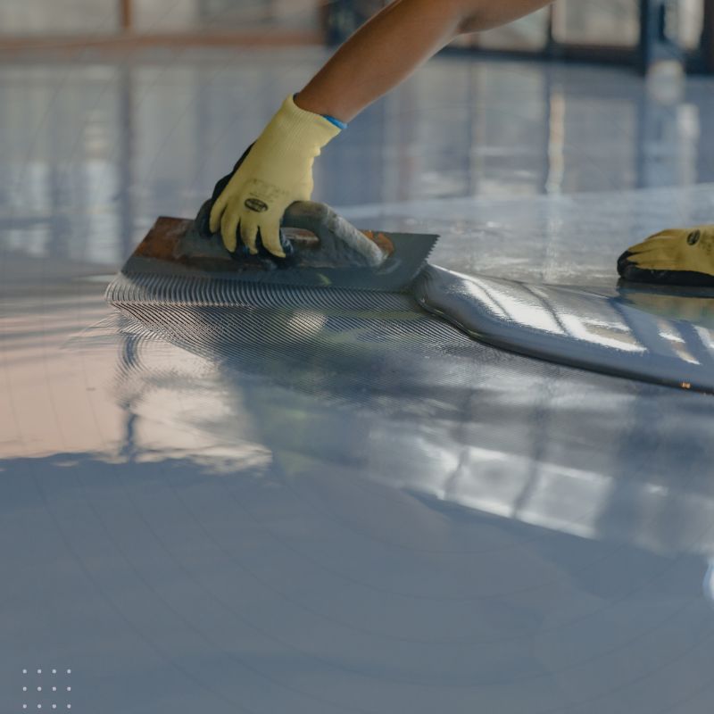 Worker applying gray epoxy coating to a floor, highlighting the need for digital marketing to generate leads for epoxy flooring companies.