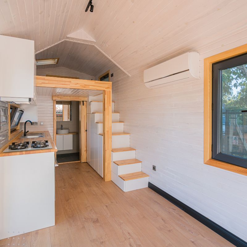 A bright and airy tiny house interior with a kitchen and stairs leading to a loft bedroom. Digital marketing for tiny home builders can help showcase your unique tiny house creations and attract potential clients.