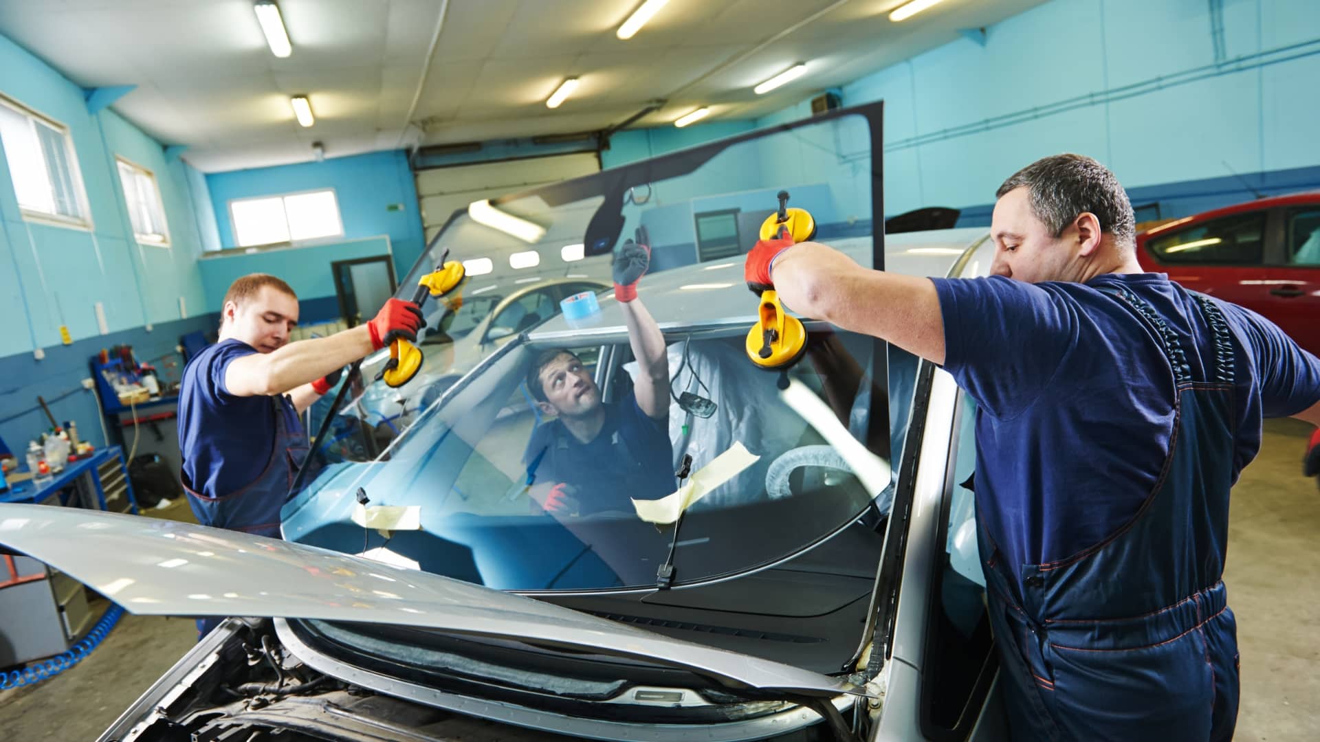 Technicians installing a new windscreen on a car inside an auto workshop